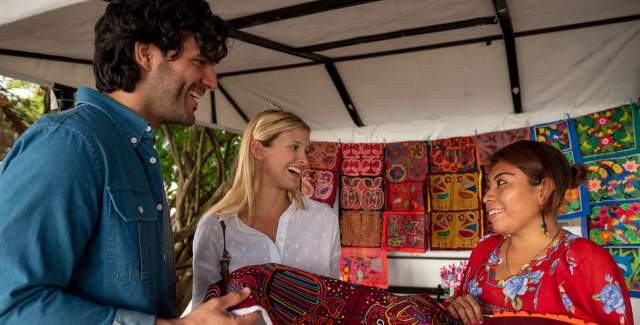Mujer de la comunidad muestra una Mola tradicional a un par de visitantes.