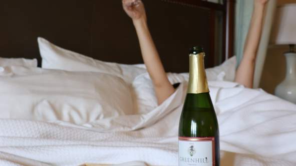 Woman relaxes in bed with sparkling wine and room service at Salamander Resort & Spa