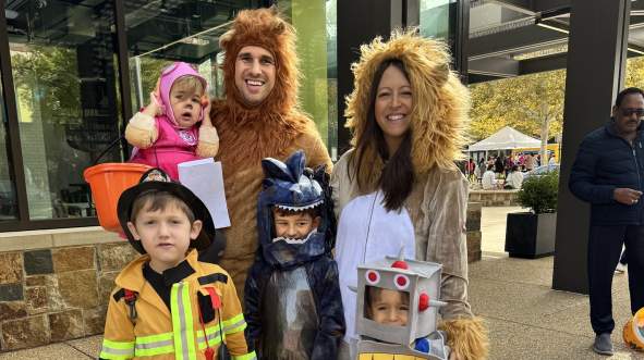 A family dressed in Halloween costumes, for the Brambleton Town Center Trick-or-Treat event, including a firefighter, a robot, a dinosaur and lion parents.