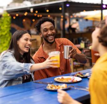 Two women and a man cheering drinks over plates of tacos.