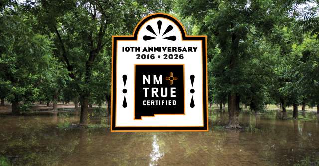 A forested area with partially submerged trees in floodwater is shown. There is a large logo displayed in the center, celebrating the 10th anniversary of "NM True Certified" from 2016 to 2026.