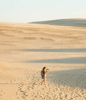 Woman walking in dunes and taking photos