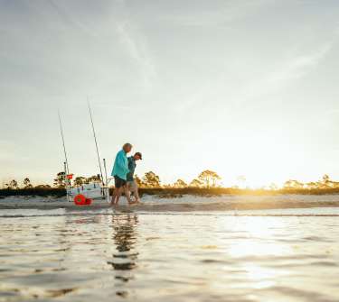 Two men walk along the shoreline at sunrise pulling a fishing cart
