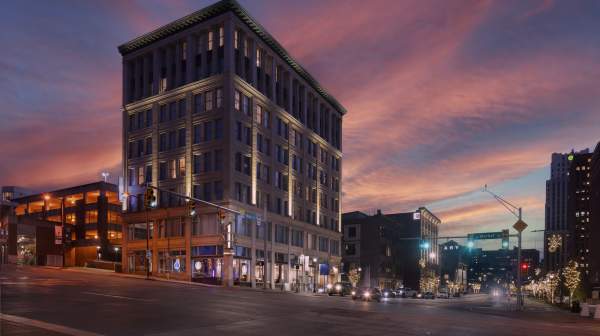 The illuminated Hotel BLU, a historic downtown building, stands on a city street corner beneath a vibrant pink and purple sunset sky.