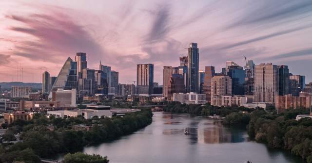 View of the Austin city skyline over Lady Bird Lake with pink and purple sky at sunset and a tour boat on the water below