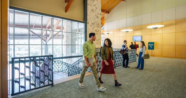 Image of a group of people dressed in business casual walking into the Palmer Events Center and chatting with one another.