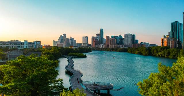 People walking along suspended board walk that follows the shape of the Colorado River, leading to Downtown Austin skyline.