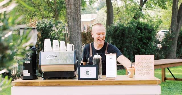 Man standing behind an event bar happily making specialty lattes.