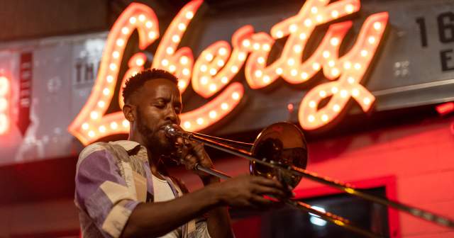 Austin musician Daniel Fears plays the trombone in front of The Liberty bar's lighted sign