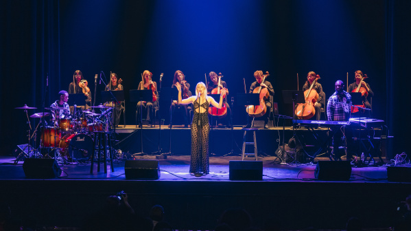 Grace Weber singing at a stand up mic with a string octet behind her