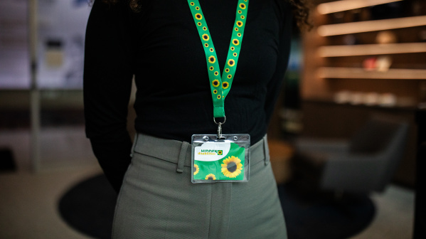 a person wears a sunflower-patterned Hidden Disability Sunflower lanyard with a badge over a black shirt and grey slacks