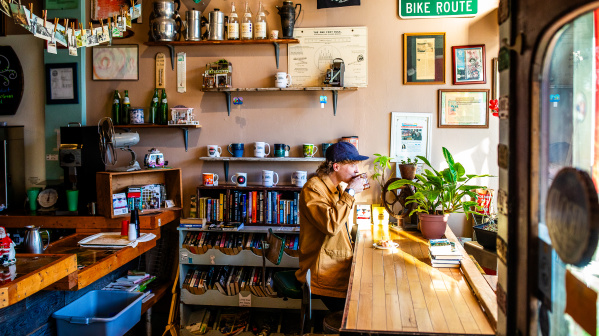 side view of a person sitting at a window drinking a cup of coffee at Sprocket Cafe