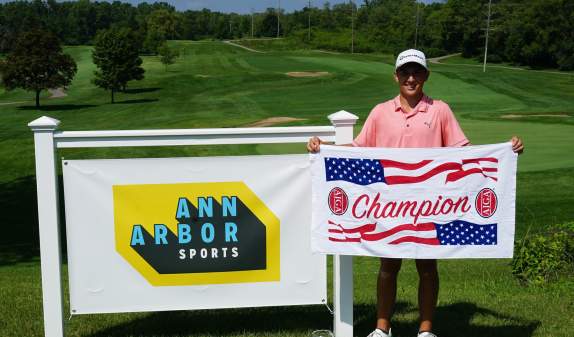 Young golfer folding championship banner next to Ann Arbor Sports logo
