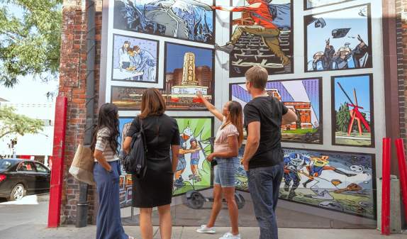 Four people admiring a public outdoor mural on the side of a bulding in downtown Ann Arbor