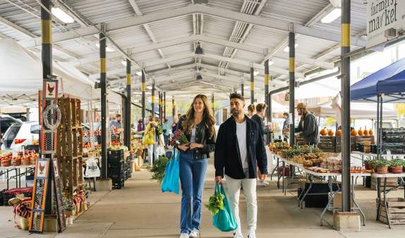 Young couple with shopping totes walking through the Ann Arbor Farmers Market