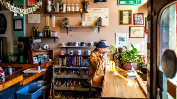 side view of a person sitting at a window drinking a cup of coffee at Sprocket Cafe