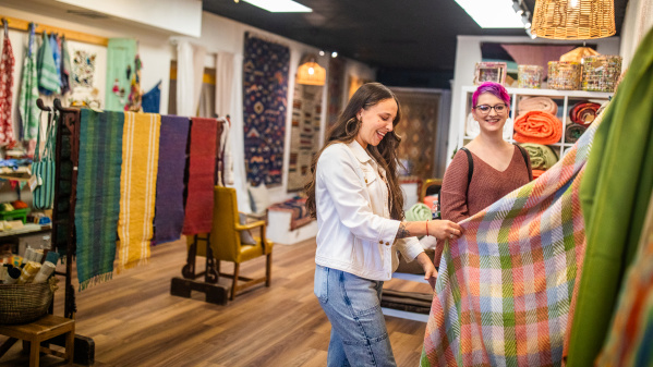 Two women examining a colorful woven textile in a bright fabric at Cultural Cloth.
