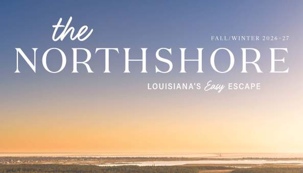 Aerial sunset view of a winding Slidell waterway bordered by homes, marshes and trees, with Lake Pontchartrain stretching across the horizon on the Fall/Winter 2026–27 cover of The Northshore.