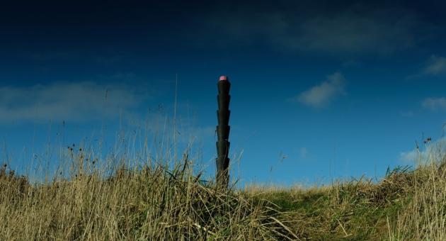 A black active beacon photopost sat within a grassed area with blue skies above.