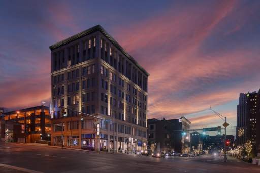 The illuminated Hotel BLU, a historic downtown building, stands on a city street corner beneath a vibrant pink and purple sunset sky.