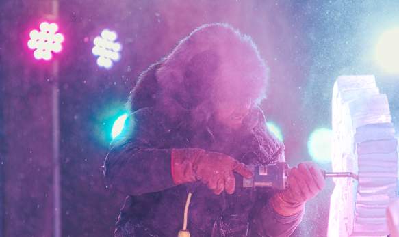 An ice carver using a power tool to carve a sculpture during the Freezefest ice battle
