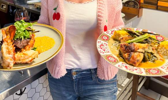Image of a woman in a kitchen smiling holding two large plates of food