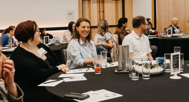 People sitting at a conference table with smiles on their faces, interacting in a conversation.
