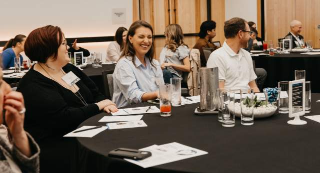People sitting at a conference table with smiles on their faces, interacting in a conversation.