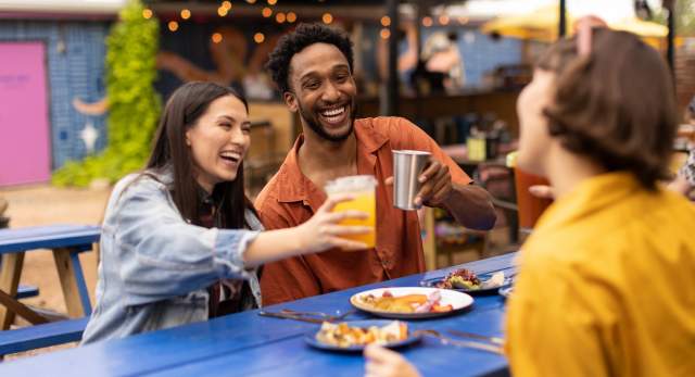 Two women and a man cheering drinks over plates of tacos.