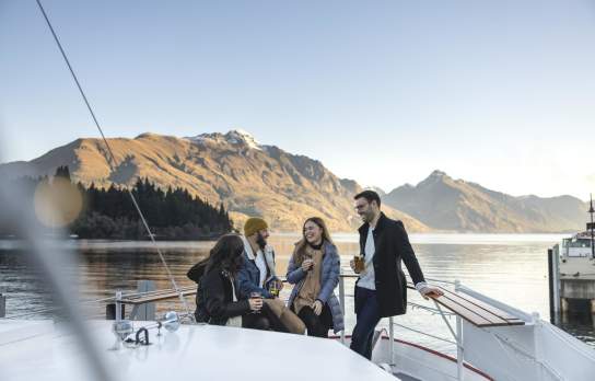Friends sitting together at a bar on a boat with still lake and mountains in the background