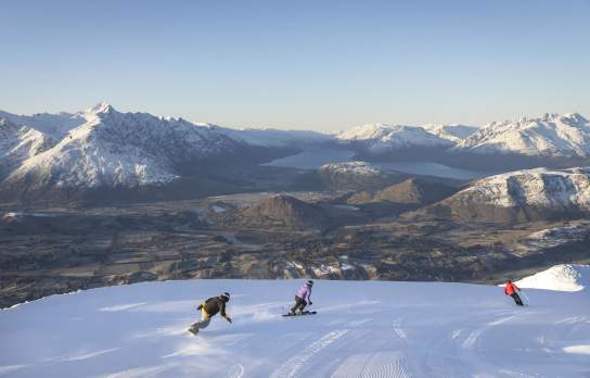 Three snowboarders riding down snowy mountain