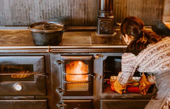 Woman cooking meal in cast iron pot over fire at The Great Glenorchy Alpine Base Camp restaurant