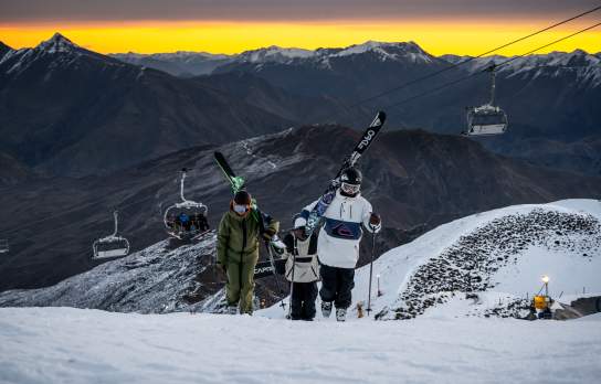 Skiers walking up mountain at Coronet Peak Night Ski during sunset
