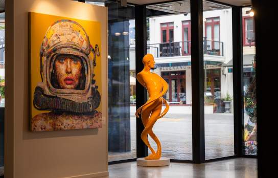 A sculpture and artwork inside a gallery with views of the street through the windows