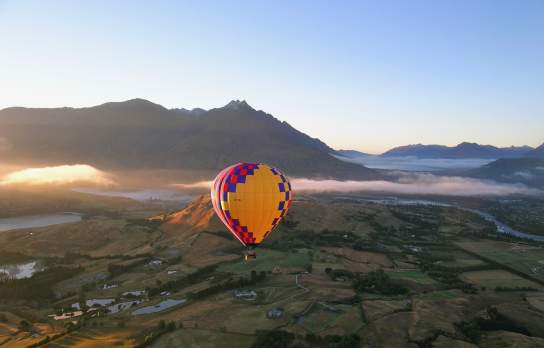 Shot of a hot air balloon at sunrise overlooking a green valley and mountain