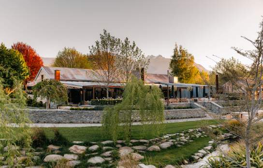 Exterior of The Woolshed Restaurant, Ayrburn with autumn coloured trees and distant mountains in the background