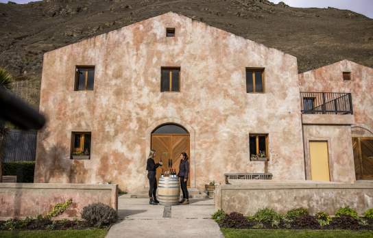 A person having a wine tasting outside Chard Farm Cellar door, a dusty pink Mediterranean style building