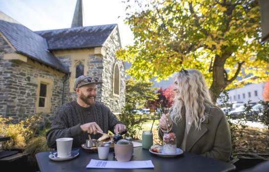 two people dining outside with a tree and church in the background