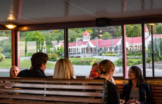A group of people sitting on the TSS Earnslaw with a view of Walter Peak through the windows