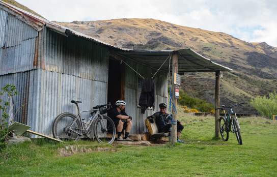 Two men taking a rest at a rugged tin back country hut with mountain bikes