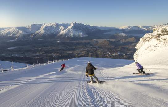 Snowboarders and skiers riding down snowy mountain