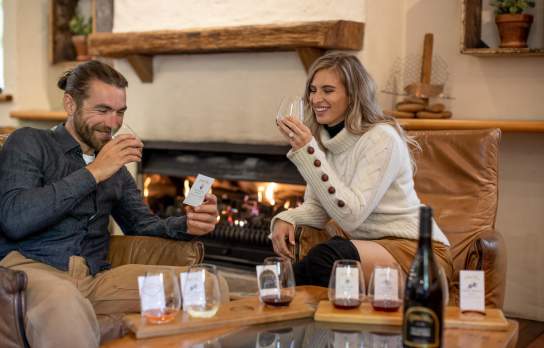 A couple tasting wine with a cosy fire in the background