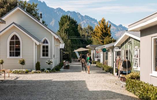A lady walking a horse on a path lined with boutique cabins and shops
