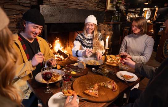 Group of friends eating at a cosy restaurant with fire roaring in the background