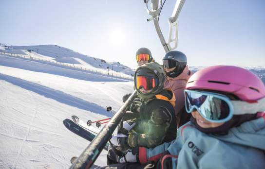 Family in ski gear sitting on a chair lift at Cardrona Ski Resort