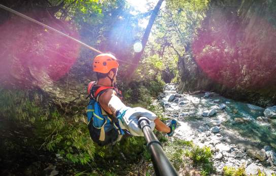 Person ziplining through a forest, over a river