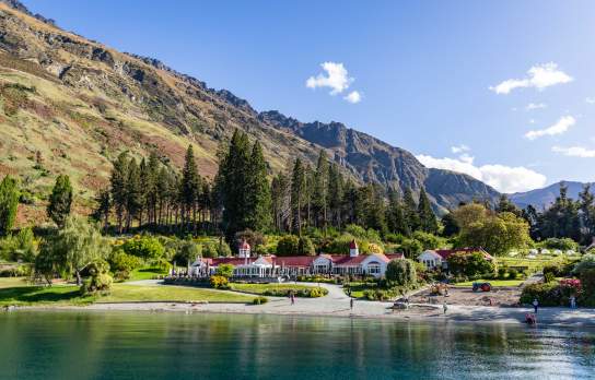 Image of Walter Peak farm house surrounded by green gardens with blue lake in the front and mountains in the background