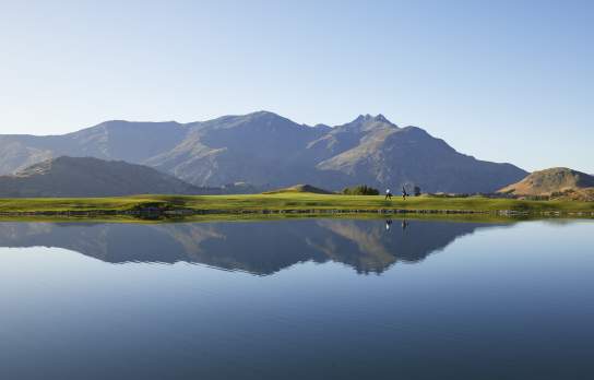 Wide shot of a golf course with lake reflecting mountains