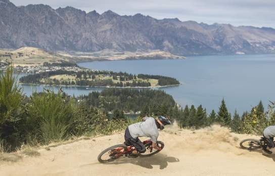 Person biking Queenstown Bike Park with view overlooking lake Whakatipu and the Remarkables mountain ranges