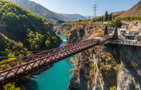 People biking over a bridge with vibrant blue water below